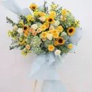 A grand floral arrangement with sunflowers, roses, and hydrangeas in yellow and light blue wrapping.