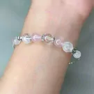A delicate bracelet with rose quartz, clear quartz beads, and silver charms on a wrist.