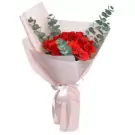 Bouquet of red roses and eucalyptus in pink paper with a white ribbon.