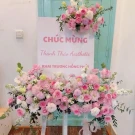 Floral arrangement with pink roses, delphiniums, and greenery on a sign.