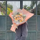 Peach and pink rose bouquet with greenery, held by a person with their face obscured.