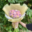 Pink and cream roses, carnations, and baby's breath bouquet with a teddy bear, wrapped in yellow paper.