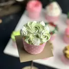 A pale green cupcake decorated with swirls of frosting, meringues, and silver sprinkles.