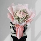 Pink roses and baby's breath bouquet wrapped in pale pink paper, tied with a pink ribbon.