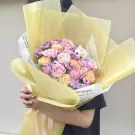 Pink and yellow roses, carnations, and baby's breath in a yellow bouquet wrap with a small white bear.