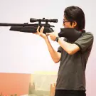 Man aims a scoped rifle in a shooting range.