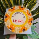 Birthday cake with "Mẹ Bơ" and "happy birthday" written on it, decorated with sunflowers.
