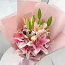 Pink and white lilies in a light pink bouquet wrap with green buds.