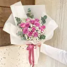 Pink roses and baby's breath bouquet wrapped in white paper with a pink ribbon.