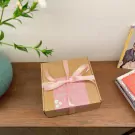 Brown gift box with pink ribbon and floral sticker, on a wooden table.