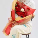 Red and yellow wrapping around a bouquet of red roses and carnations with a white pom-pom flower.