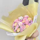 Pink roses and carnations arranged in a bouquet with a teddy bear, wrapped in yellow paper.