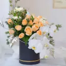 Peach roses and white orchids in a black box, with silver-dusted ferns.