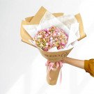 Pink hydrangea bouquet wrapped in brown paper with a pink ribbon, held by a hand.