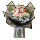 Pink roses, baby's breath, and red berries in a black paper bouquet with a white ribbon.