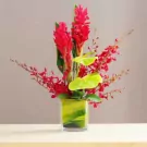 Red Mokara orchids with pink anthurium and other red flowers in a square glass vase.