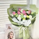 Pink lotus bouquet with green lotus pods, white carnations, and pink eustoma, wrapped in light green paper with a white ribbon.