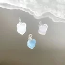 Three heart-shaped stone pendants, clear quartz, rose quartz, and aquamarine, on a mirrored surface.