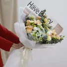 Bouquet of peach roses, hydrangeas, and carnations wrapped in white paper, with a newspaper accent.