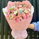 Pink roses, carnations, and white daisies in a pink bouquet with a white ribbon.