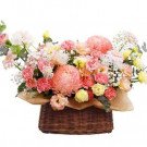 Pink and yellow flowers in a brown woven basket, including chrysanthemums, carnations, and asters.