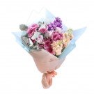 A romantic bouquet of purple and pink roses, chrysanthemums, and delphiniums, wrapped in light blue and peach paper, tied with a ribbon.