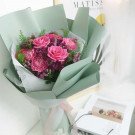 Pink roses, carnations, and purple chrysanthemums in a light green bouquet wrapper.