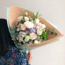 Pastel flower bouquet with roses, eustomas, and hydrangeas, wrapped in brown paper.