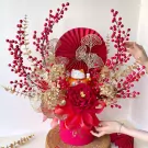Lucky cat in a red flower box with gold accents and red berries, a symbol of prosperity.