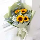 A bouquet of sunflowers and baby's breath, wrapped in pale green paper, tied with a white ribbon.