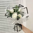 Bouquet of white roses with eucalyptus, wrapped in clear paper with black trim and ribbon.