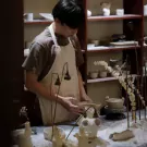 Potter working at a clay pottery workshop with shelves of ceramics.