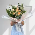 Bouquet of orange roses and greenery wrapped in white and pink paper with grey ribbon.