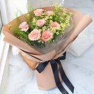 Pink roses and daisies in a bouquet wrapped in brown paper with a black ribbon.