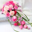 Pink and cream cascade wedding bouquet with roses and small purple flowers.