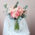 A bouquet of pink and cream roses with eucalyptus leaves in a clear glass vase.