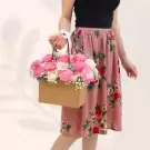 Woman holding a floral arrangement in a box with pink and cream roses.
