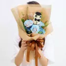 Bouquet with blue roses, hydrangeas, and a white figure dressed as a teacher, wrapped in brown paper and tied with a ribbon.