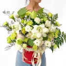 A person holds a red box filled with white lotus, green carnations, lisianthus, and lotus seed pods.