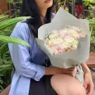 Woman holding a bouquet of pink and white roses with baby's breath, wrapped in light blue paper.