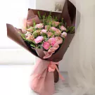 Pink and peach roses and carnations in a bouquet wrapped in brown and pink paper.