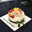 White mousse cake with fruit and a July calendar design, decorated with a green ribbon.