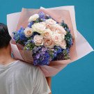 Man carrying a bouquet of white and pink roses with blue hydrangeas.
