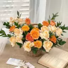 Basket of orange and cream roses with greenery, next to open books.