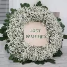 Wedding car wreath with "Just Married" banner, made of baby's breath and greenery.