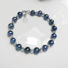 A dark blue pearl bracelet with silver accents and a clover charm.
