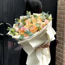 A woman in black holds a large bouquet of peach and pink roses, lisianthus, and chrysanthemum.