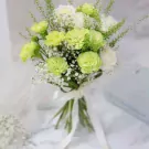 Bridal bouquet with green carnations, white roses, and baby's breath tied with a white ribbon.