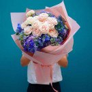 Bouquet of pink roses and blue hydrangeas, wrapped in pink paper.
