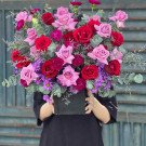 Pastel purple and red rose floral arrangement in a black box held by a person in a black dress.